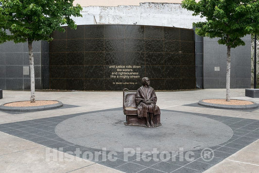 Photograph- A life-size bronze statue of African-American civil-rights stalwart Rosa Parks, sitting on a bus bench, the focal point of a plaza at a Dallas Area Rapid Transit, or DART, station
