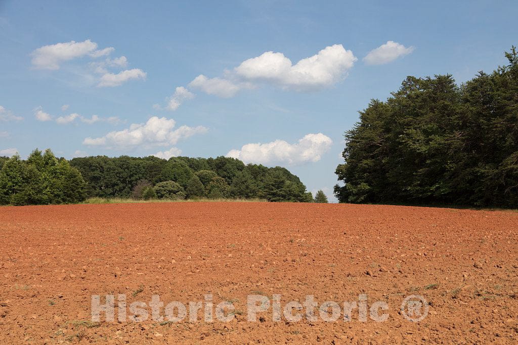 Photo - A Plowed Field of red-Clay Soil Stands in Sharp Contrast to The Surrounding Lush Green Trees and Blue Sky Overhead in Rockingham County, North Carolina