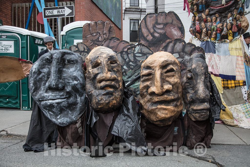 Photograph- Large, bizarre puppet masks from the Bread and Puppet Theater, a politically radical theater and sourdough-bread bakery in tiny Glover, Vermont, are displayed while members of the